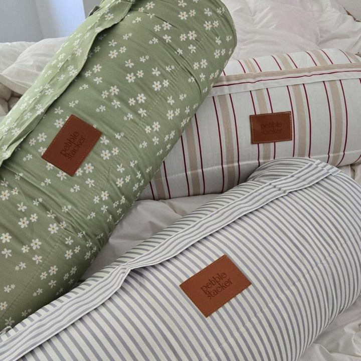 Three pillows with floral and striped patterns on a bed, featuring a brand label.
